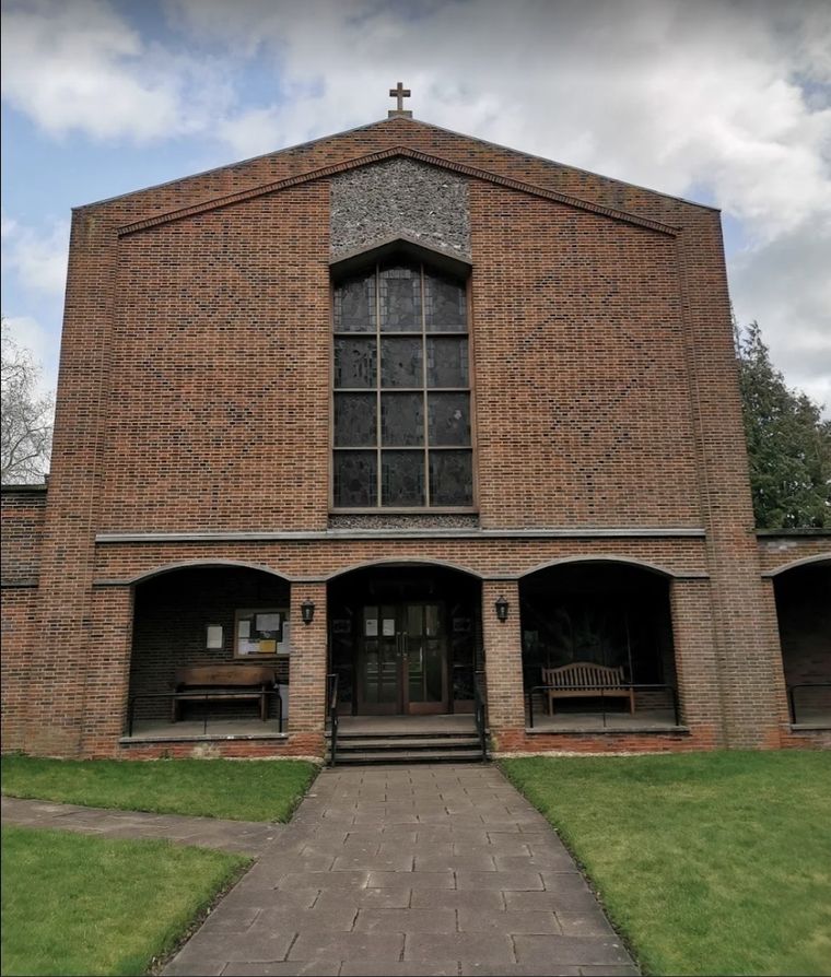 The brick front of St Hugh of Lincoln church, with a tall stained glass window above three arched entrances